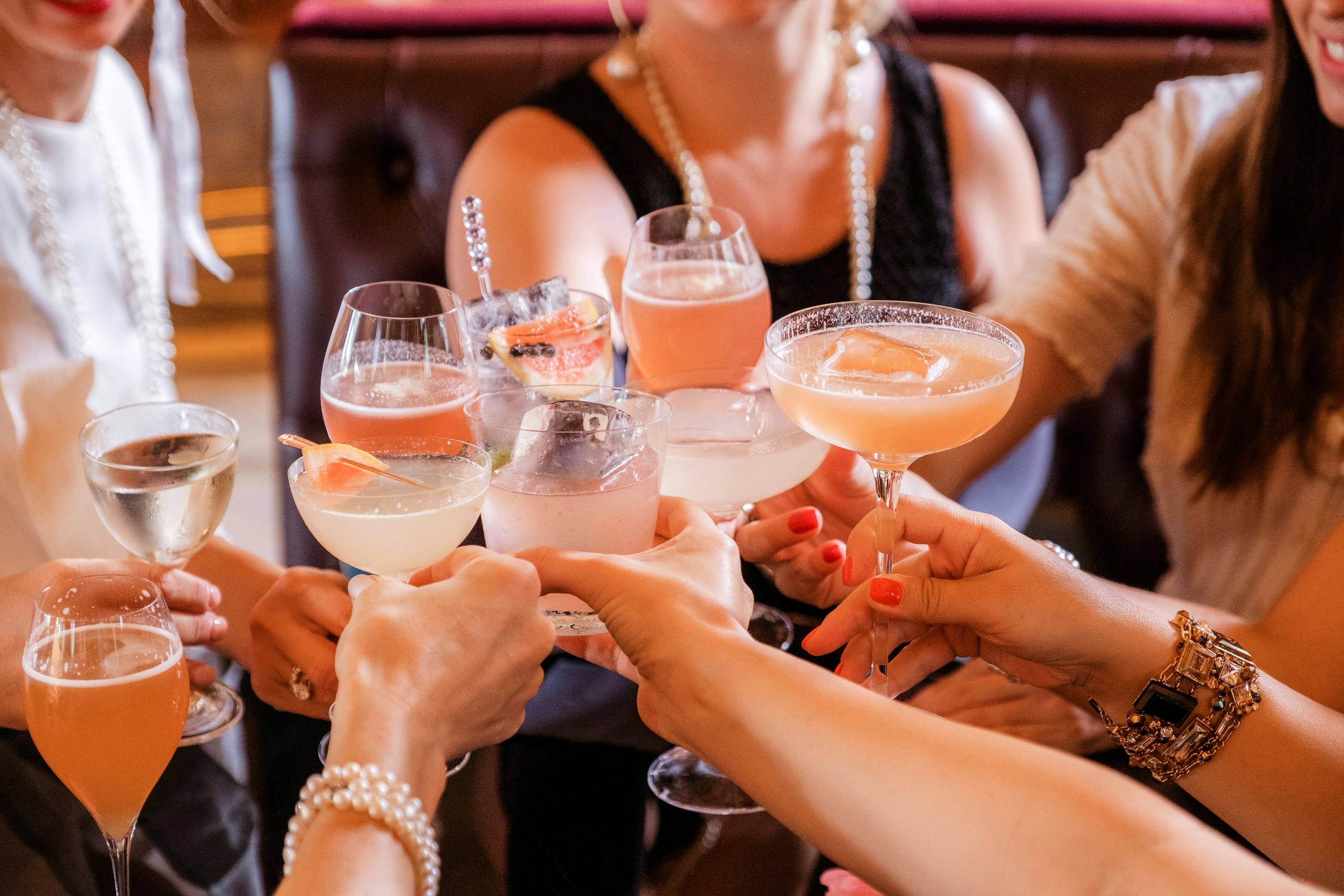 Varias manos brindando con copas de vino rosado en la mesa de un bar
